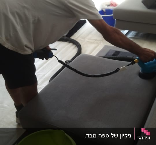 אדם מנקה ספה עם מכשיר חשמלי ודלי סבון